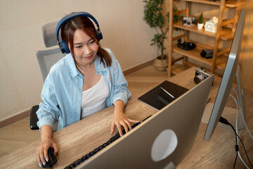 Asian woman holding a camera and using application video editor works on the computer with footage on wooden table.