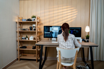 Female asian freelancer editing video for customer or travel blogger in program on computer while sitting at the table and working at home