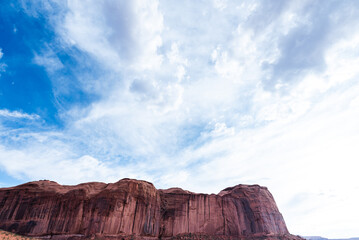 Expansive sky over towering red rock cliffs in Monument Valley desert.