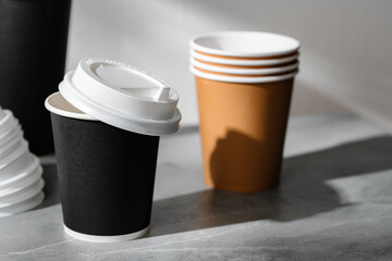 Stack of coffee cups in various colors with lids on a gray surface