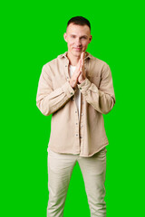 Young Man Wearing Beige Jacket and Pants Standing With Hands Together Against Bright Green Background