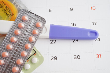 Pregnancy test with birth control pills and condom for female on calendar, ovulation day.