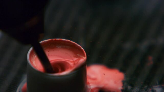 Clouseup of tattoo artist mixing red ink in caps fixed with vaseline on table. Tattooist preparation, flow of dark fluid dye in container. Master tattooer loads flask with ebony paint liquid.