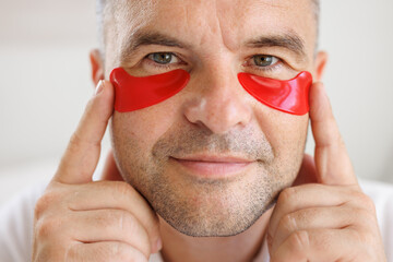 Man applying eye patches to face. Wrinkles and facial care at home for men.