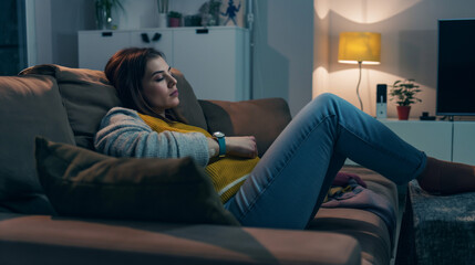 Obraz premium Young woman resting her head on a couch, in a dimly lit cozy room, looking introspective.