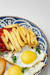 Breakfast plate with fried eggs, sausage, tomatoes, and fries served on a decorative blue plate