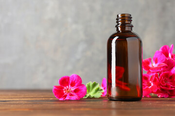 Geranium essential oil in bottle and beautiful flowers on wooden table, space for text