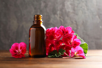 Geranium essential oil in bottle and beautiful flowers on wooden table