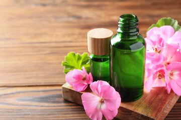 Geranium essential oil in bottles and beautiful flowers on wooden table, space for text