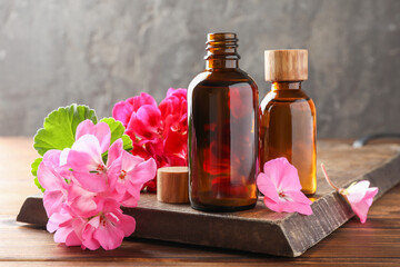 Geranium essential oil in bottles and beautiful flowers on wooden table