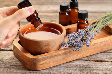 Woman dripping essential oil into bowl with water at wooden table, closeup