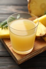Tasty pineapple juice in glass and slices of fresh fruit on wooden table, closeup