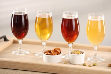 Glasses with different types of beer and snacks on wooden table indoors, closeup
