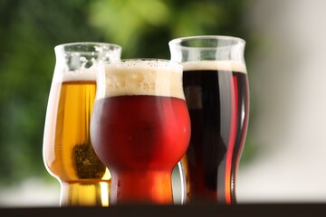Glasses with different types of beer on table against blurred background, closeup