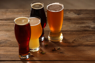 Glasses with different types of beer and pistachio nuts on wooden table