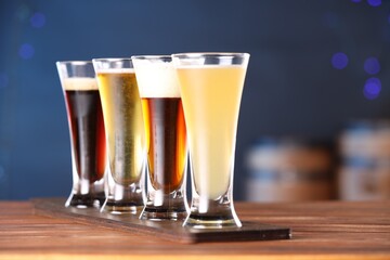 Glasses with different types of beer on wooden table against blue background, closeup