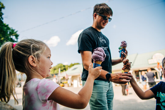 A young girl holds an ice cream cone with an adult and another child