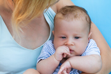 A young child, dressed in stripes, gently sucks on his thumb while being held by a loving parent. The warm sunlight enhances their tender moment.