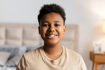 Portrait of smiling African American boy sitting in his bedroom at home