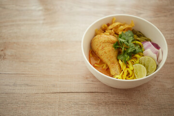 Rice noodle with chicken and curry in white bowl on wooden background, Khao soi a famous northern Thai food