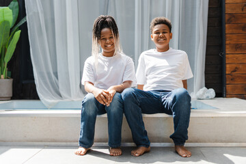 Happy young African American kids embracing together, sitting near swimming pool