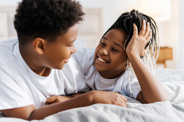 Happy two kids talking, looking each other, lying on the bed at home