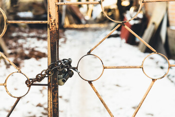 Rusty old metal gate with lock. In gloomy winter weather, a metal lock hangs on an old abandoned gate.