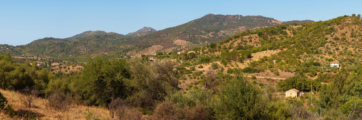 Obraz premium A panoramic view of a rural mountain landscape with rolling hills, scattered trees, and distant homes under a clear blue sky, highlighting the serene beauty of the countryside