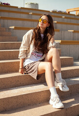 hipster girl in sunglasses sitting on stairs and smiling