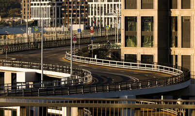 An empty road curves through a city. A wide, empty road curves around a tall building in an urban area. The road is surrounded by metal railings and the building has many windows.