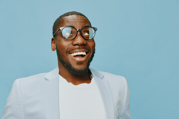 Happy young man wearing glasses smiling against a blue background, exuding confidence and joy,...