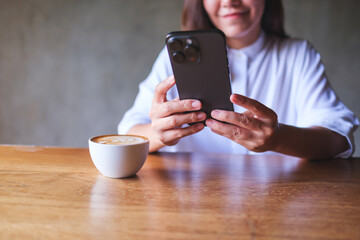 Closeup image of a young woman holding and using mobile phone in cafe