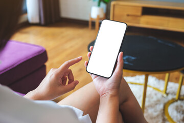 Mockup image of a woman holding mobile phone with blank desktop white screen at home