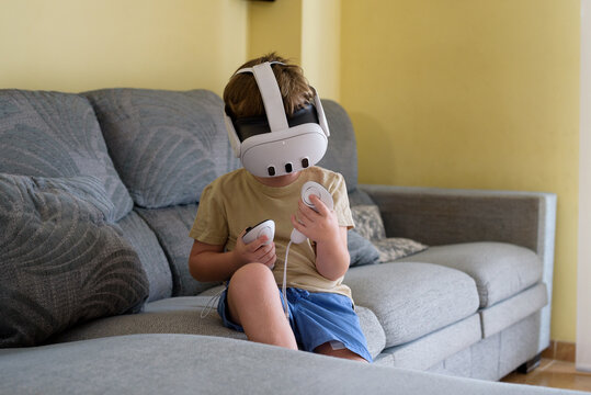 Excited child with virtual reality glasses in the living room at home. School education program for children. Surprised little boy looking with VR glasses