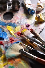 Fototapeta premium Artist's palette, brushes and paints on grey table, closeup