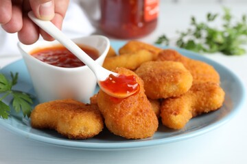 Woman eating tasty chicken nuggets with chili sauce at white table, closeup