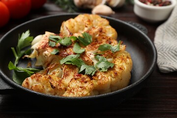 Tasty cauliflower steak and parsley in frying pan on wooden table, closeup