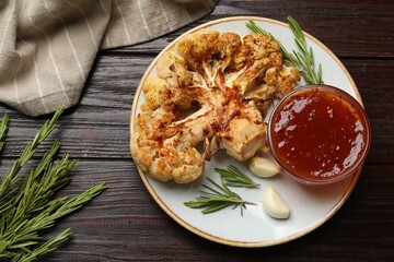 Delicious baked cauliflower steaks with sauce, garlic and rosemary on wooden table, flat lay