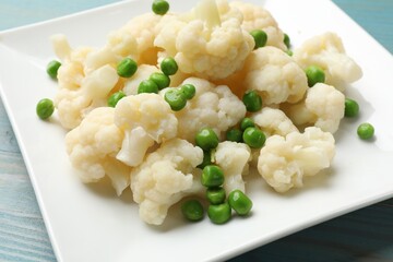 Tasty cooked cauliflower with green peas on light blue wooden table, closeup