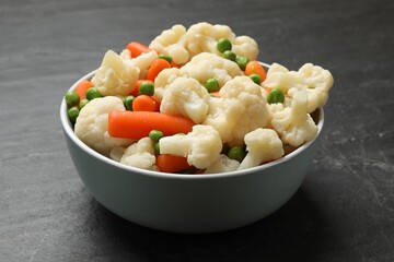 Tasty cauliflower with baby carrots and green peas on black table, closeup