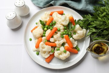 Tasty cauliflower with baby carrots and green peas on white tiled table, flat lay