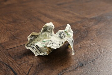 One crumpled dollar banknote on wooden table, closeup