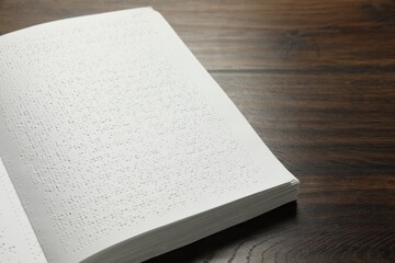 Book with Braille text on wooden table, closeup. Education and leisure for blind people