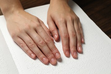 Blind woman reading book written in Braille at wooden table, closeup