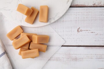 Tasty sweet caramel candies on white wooden table, flat lay. Space for text