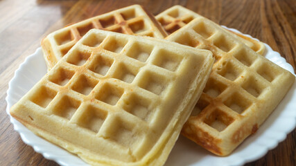 Belgian waffles on a white plate on a wooden table. Belgian waffles close-up