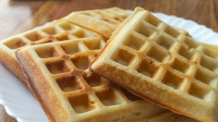 Belgian waffles on a white plate on a wooden table. Belgian waffles close-up