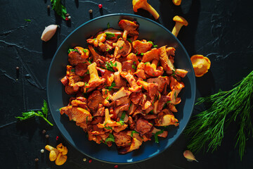 Dish with fried chanterelles, herbs and spices on black slate board.