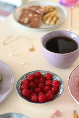 Plate of pastel macarons, cookies and chocolate, cup of tea of coffee, glass of bubble water, various berries, books and accessories on the table. Selective focus, pastel colors.