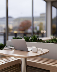 A laptop, books and headphones on a wooden table in a cozy contemporary coffee shop.